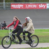 Female volunteer riding a tandem with a female participant, female handcycling riding in the background